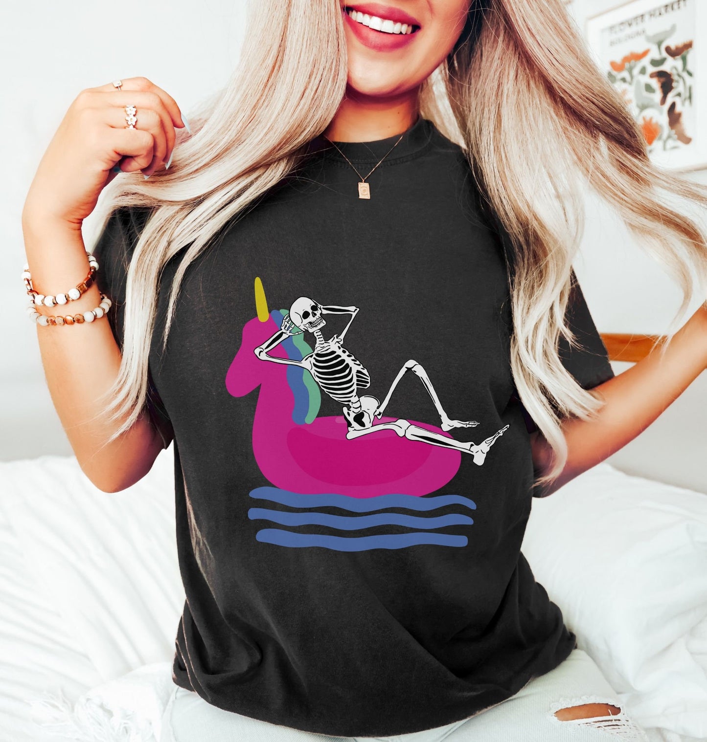 A woman wearing a vintage, black colored shirt with a smiling skeleton relaxing on a pink unicorn shaped inflatable raft, its hands behind its head relaxing and enjoying the water.