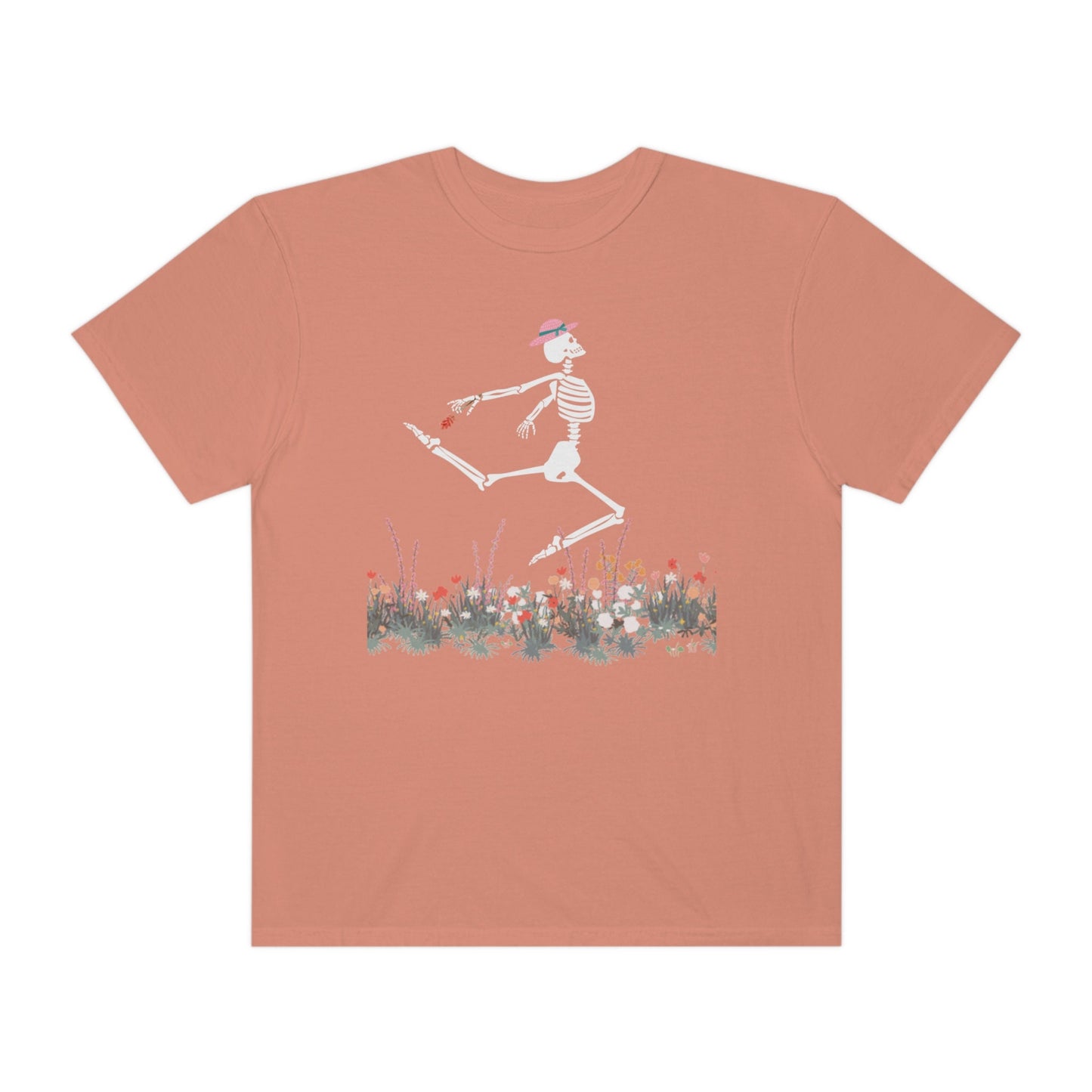 A cute orange colored shirt with a white female skeleton in a pink bonnet holding a red flower dancing in the air above a meadow of flowers.