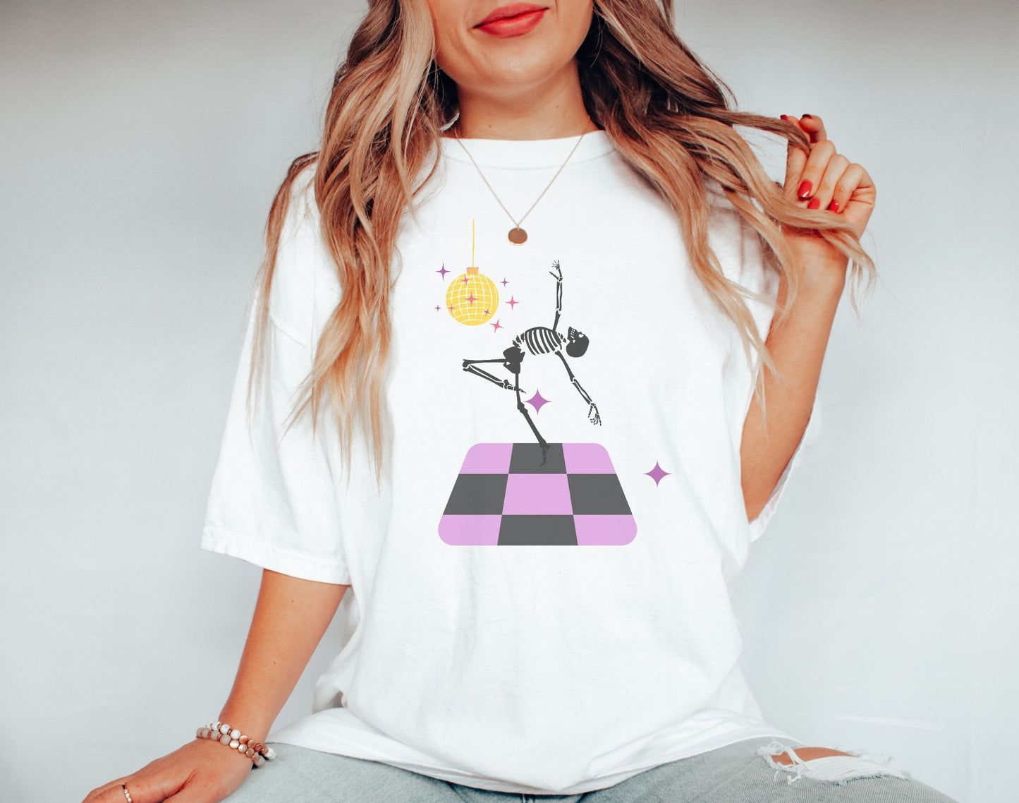 A woman wearing a cute white colored shirt with a female skeleton dancing on a black and purple dance floor under a yellow, spinning disco ball.