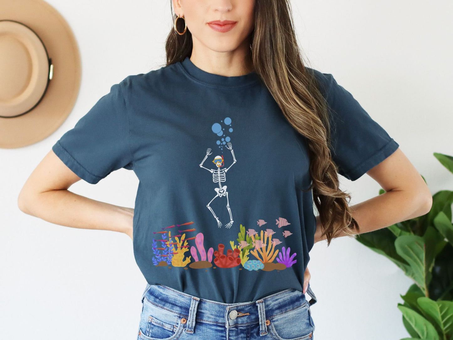 A woman wearing a vintage, navy blue colored shirt with a skeleton wearing water goggles and a snorkel under the ocean swimming among fish and colorful coral.