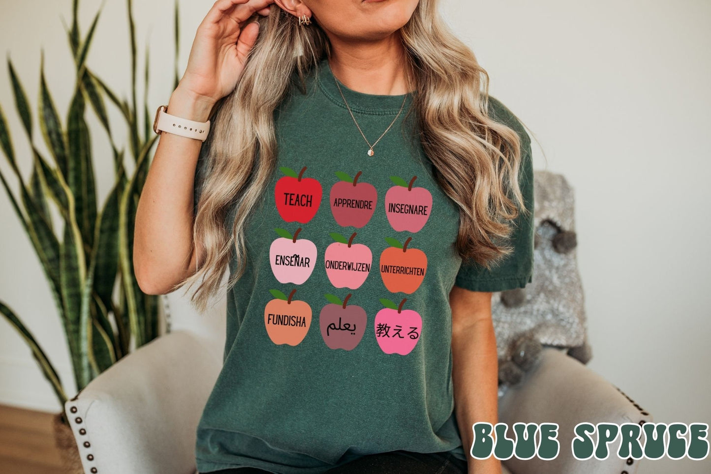 A woman wearing a vintage, blue spruce colored shirt with red, salmon, pink and orange colored apples with different variations of the word Teach in English, Spanish, French, German, Dutch, Arabic, Swahili, and Chinese.