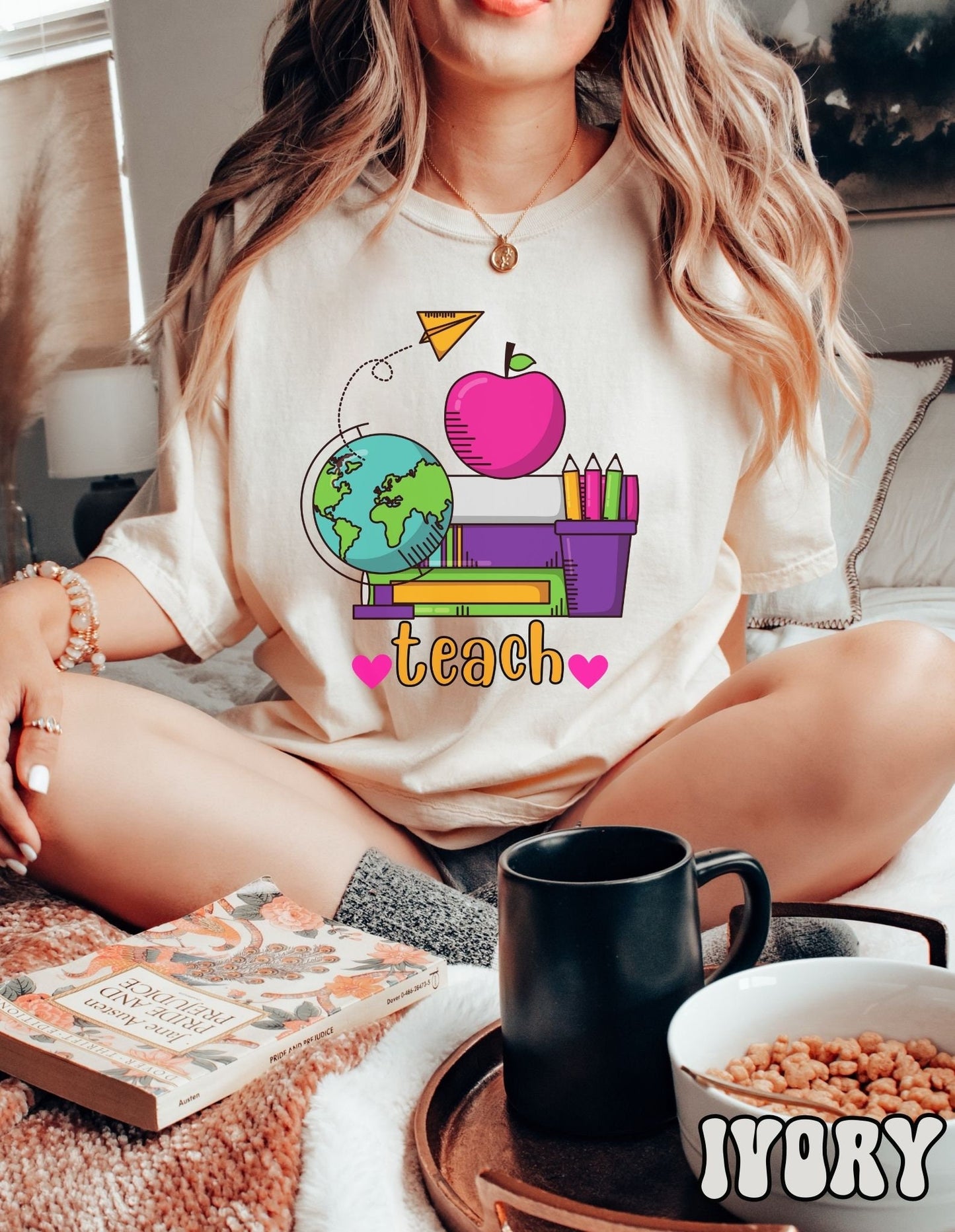 A woman wearing a vintage, ivory colored shirt with the word teach in between two pink hearts, and above are a stack of green, purple, and white books, a pink apple and a colorful pencil holder, a globe, and a yellow paper airplane flying above.