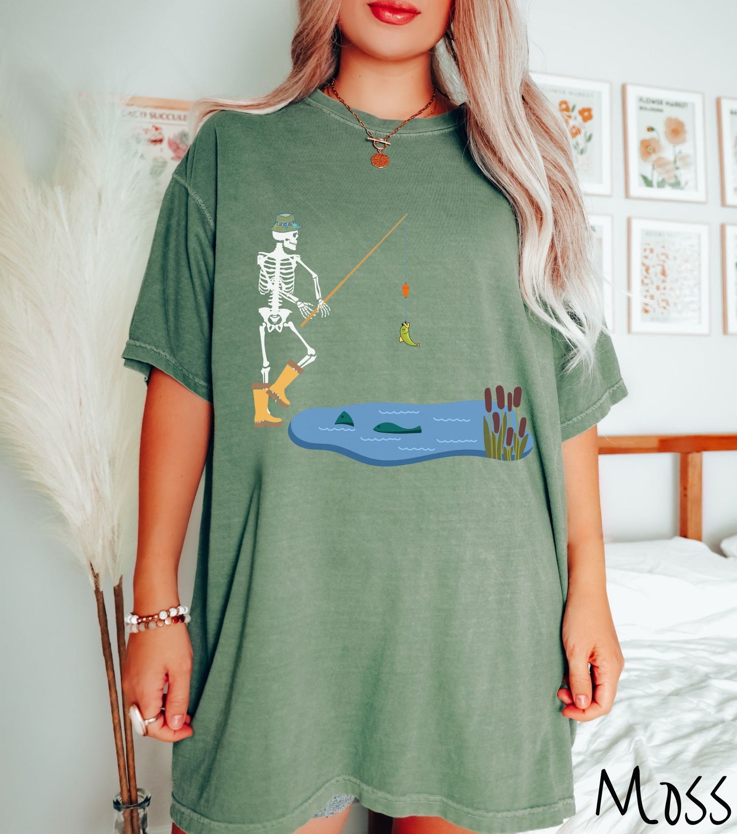 A woman wearing a cute, vintage moss colored shirt with a skeleton wearing yellow rain boots reeling in a green bass from a pond with fish swimming at the top.