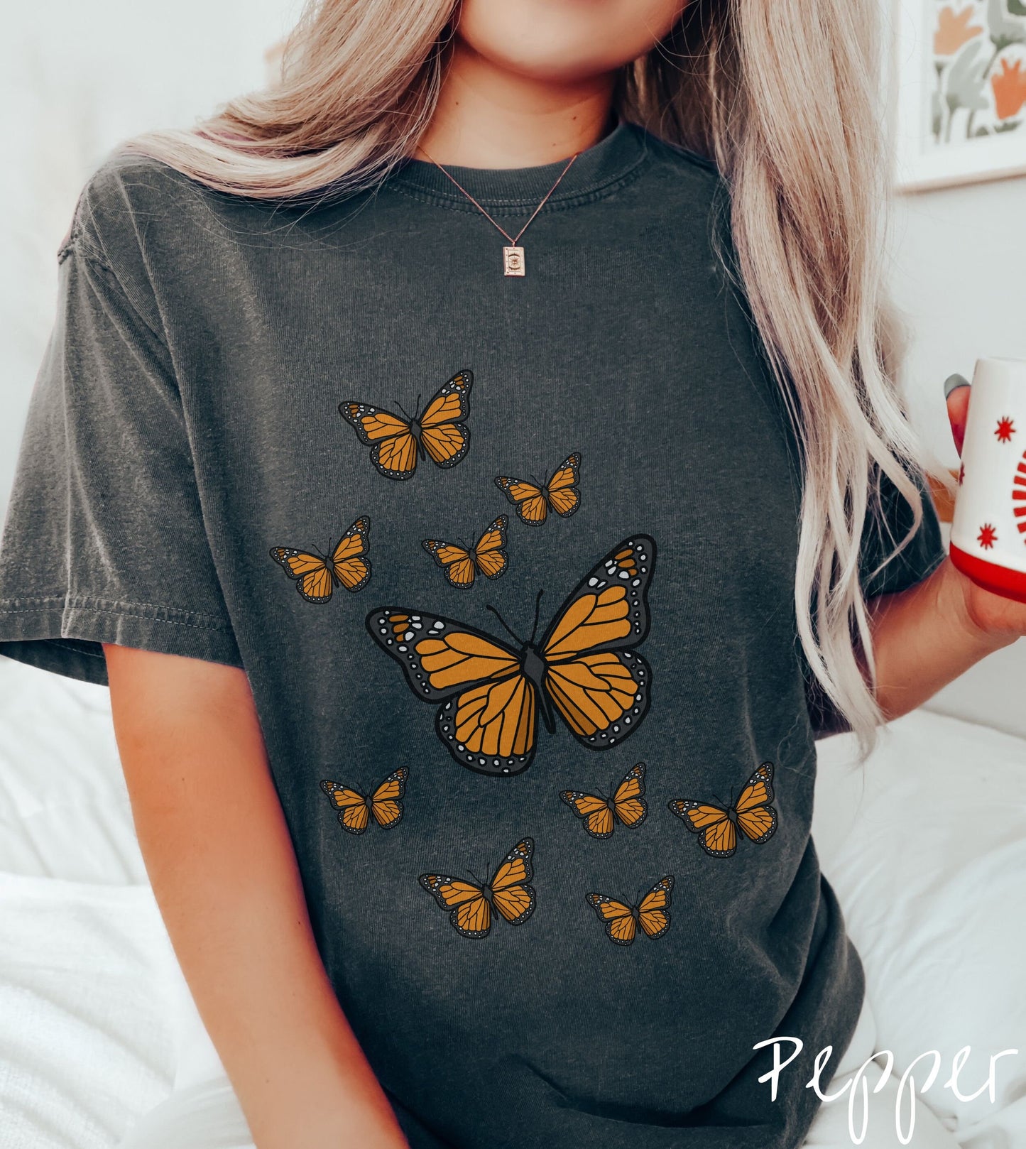 A woman wearing a vintage, pepper colored shirt with a large yellow and black butterfly in the center of the shirt and nine smaller yellow and black monarch butterflies fluttering around behind it.