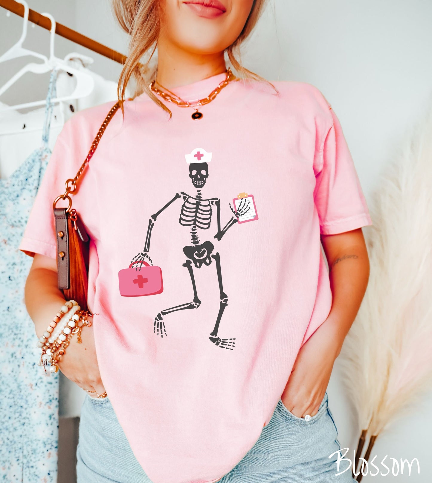 A woman wearing a cute blossom colored shirt with a female skeleton dancing wearing a nurse’s hat and carrying a pink medical bag and a pink clipboard.