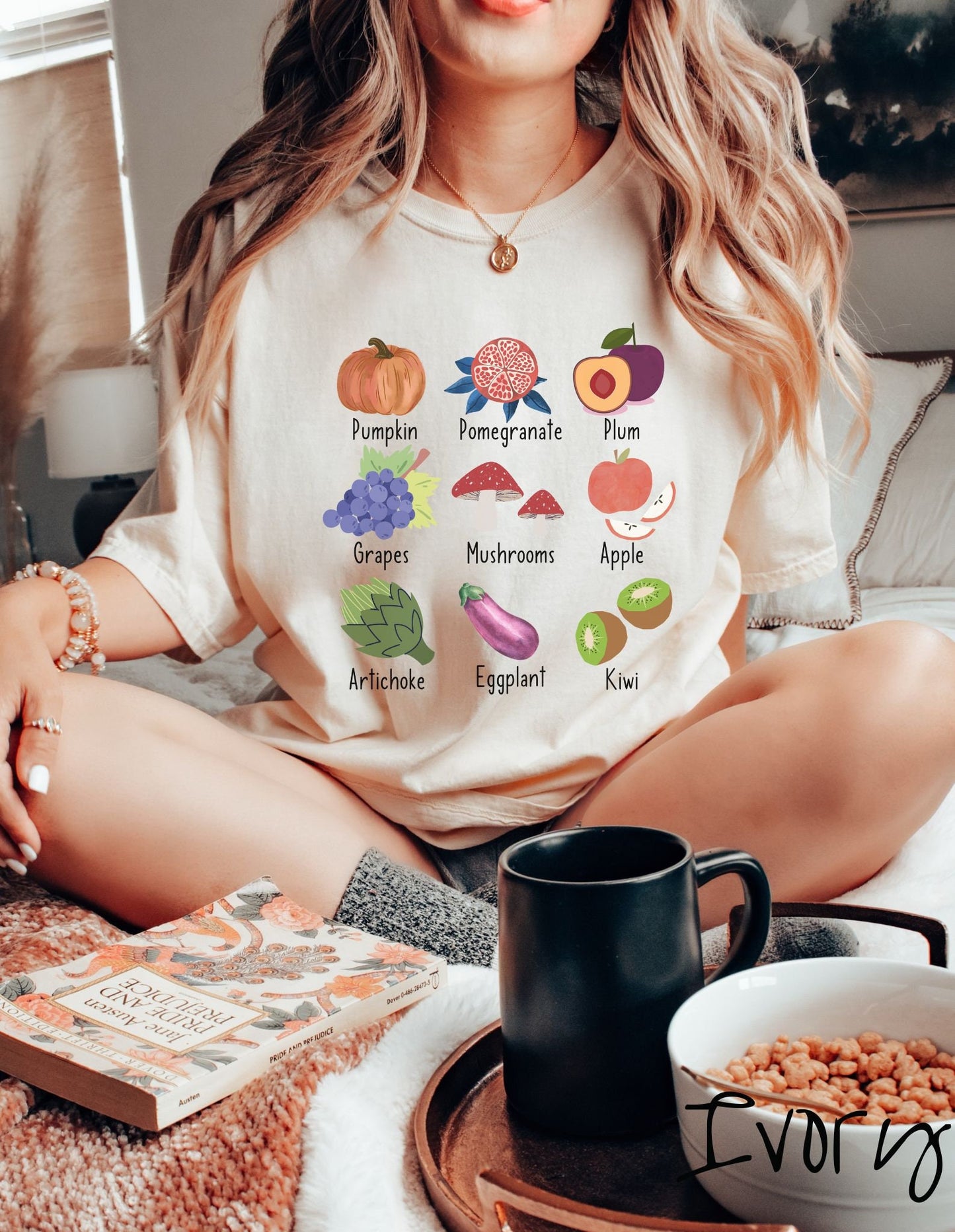 A woman wearing a vintage, ivory colored shirt with the picture and text of a pumpkin, a pomegranate, a plum, grapes, mushrooms, an apple, an artichoke, an eggplant, and a kiwi listed in three rows of three.