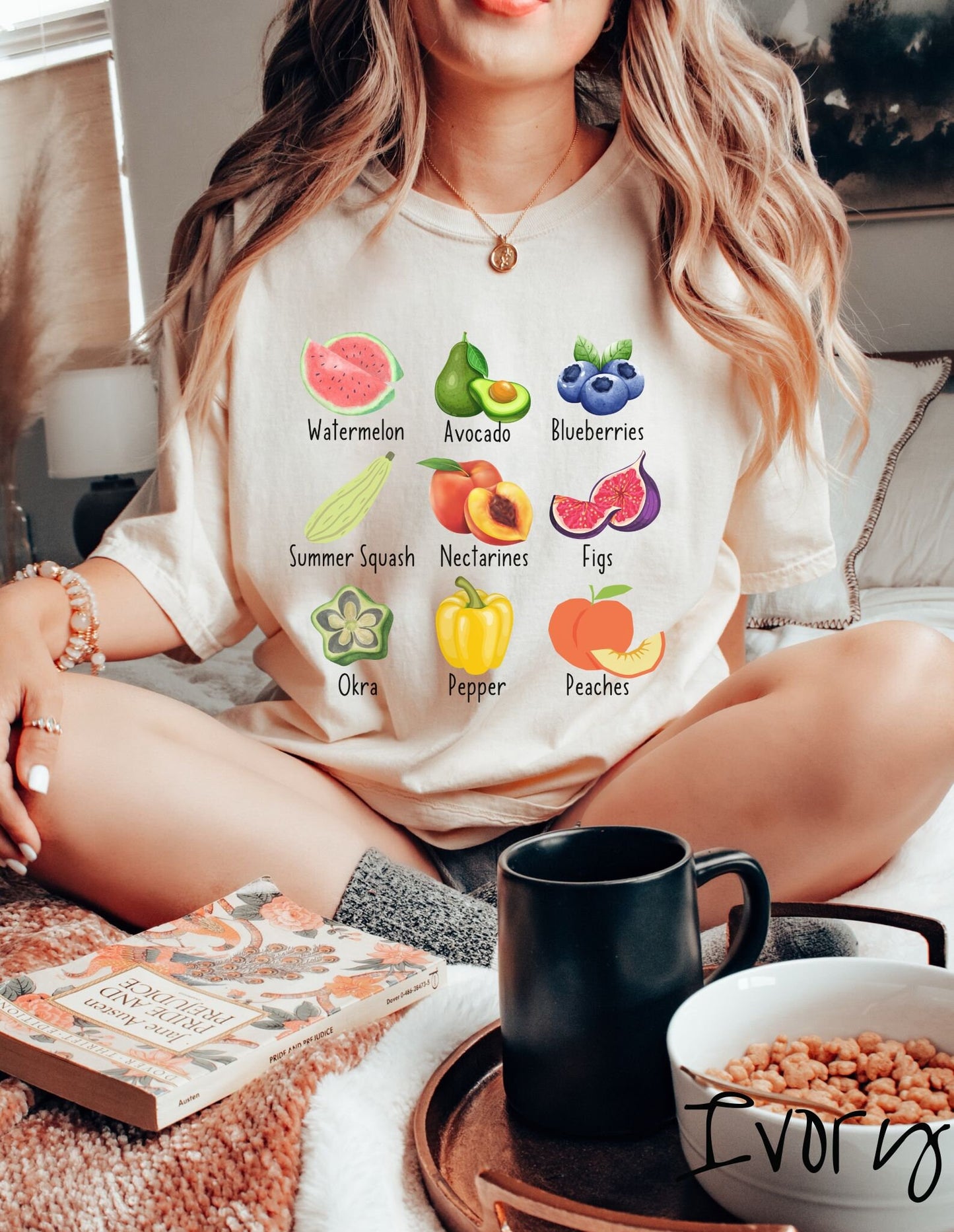 A woman wearing a vintage, ivory colored shirt with the picture and text of a watermelon, an avocado, blueberries, a summer squash, nectarines, figs, oka, a pepper, and peaches listed in three rows of three.