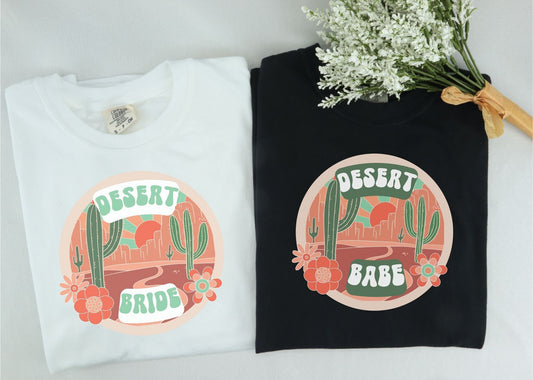 Black and white colored shirts with the text Desert Bride over an animated image of a desert road with cacti and desert flowers.
