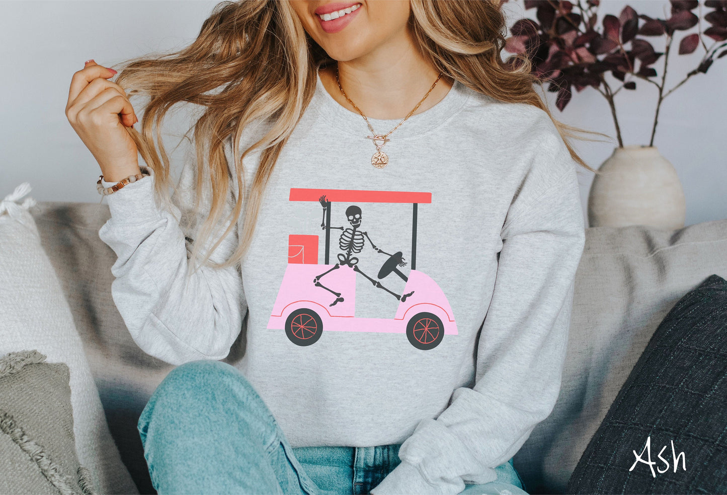A woman wearing a cute ash colored sweatshirt with a skeleton wearing a Santa hat driving a pink golf cart and waving.