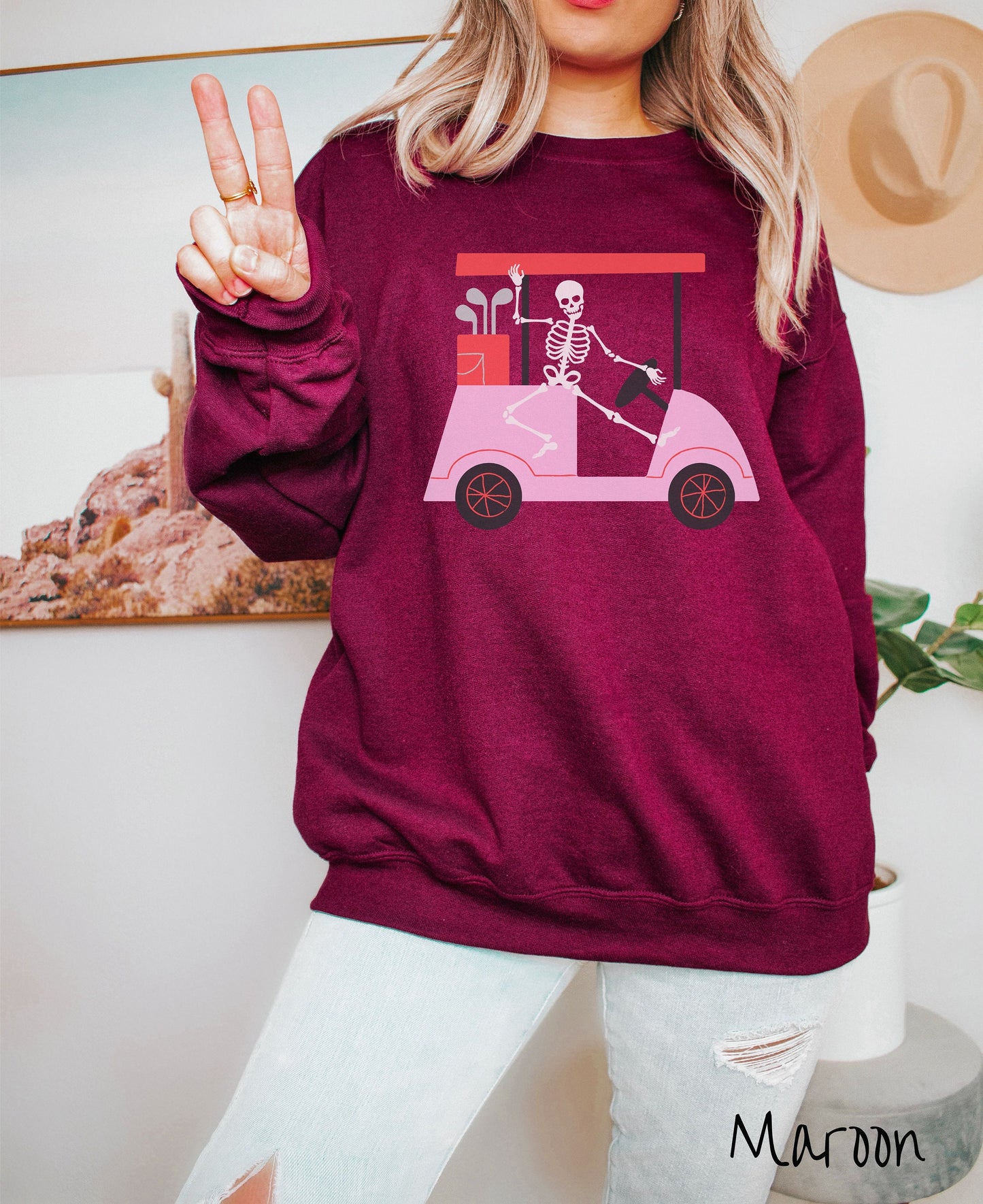 A woman wearing a cute maroon colored sweatshirt with a skeleton wearing a Santa hat driving a pink golf cart and waving.