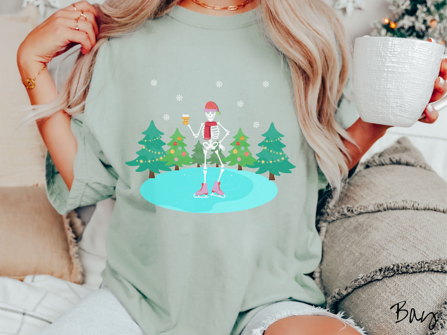 A woman wearing a vintage, bay colored shirt with a female skeleton wearing a red Santa hat, red scarf, red and pink ice skates, and holding a coffee, ice skating on a pond at night with snowflakes in the air and Christmas trees in the background.