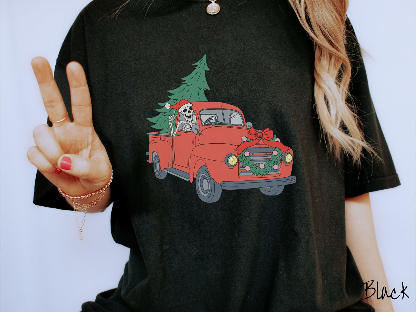 A woman wearing a cute, vintage black colored comfy sweatshirt with a skeleton wearing a Christmas santa hat driving an old red pickup truck with a Christmas tree stuffed into the back, and a wreath across the front bumper.