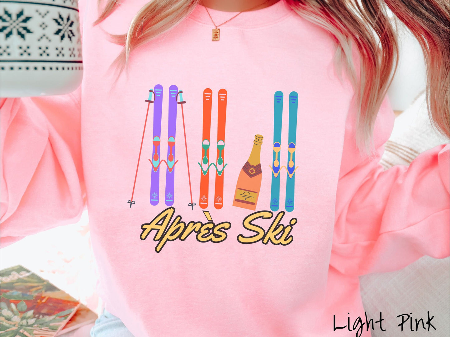 A woman wearing a vintage, light pink colored sweatshirt with sets of purple, orange, and turquoise snow skis standing upright, and a big bottle of champagne next to them. Below the skis is the text Apres Ski which is French for After Skiing.