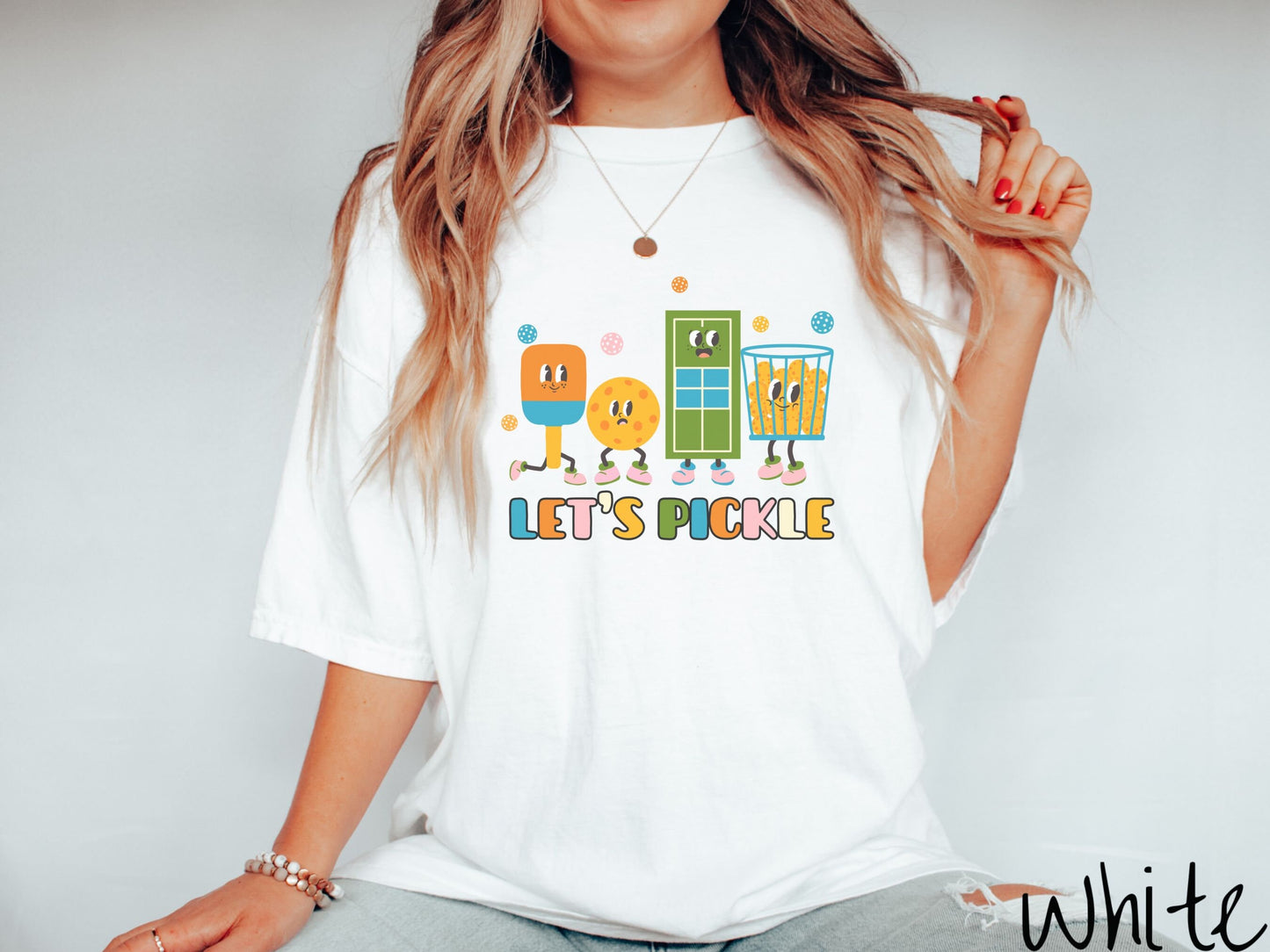 A woman wearing a cute white colored shirt with the text Let's Pickle along the bottom, and above the text are a popsicle, cookie, popcorn, and pickle balls.