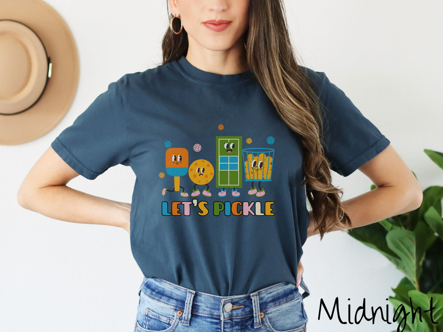 A woman wearing a cute midnight colored shirt with the text Let's Pickle along the bottom, and above the text are a popsicle, cookie, popcorn, and pickle balls.