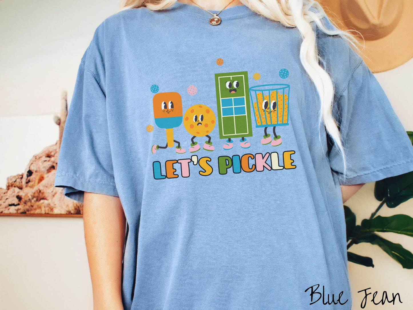 A woman wearing a cute blue jean colored shirt with the text Let's Pickle along the bottom, and above the text are a popsicle, cookie, popcorn, and pickle balls.