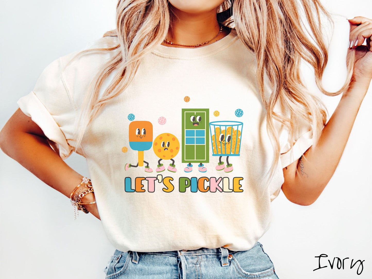 A woman wearing a cute ivory colored shirt with the text Let's Pickle along the bottom, and above the text are a popsicle, cookie, popcorn, and pickle balls.