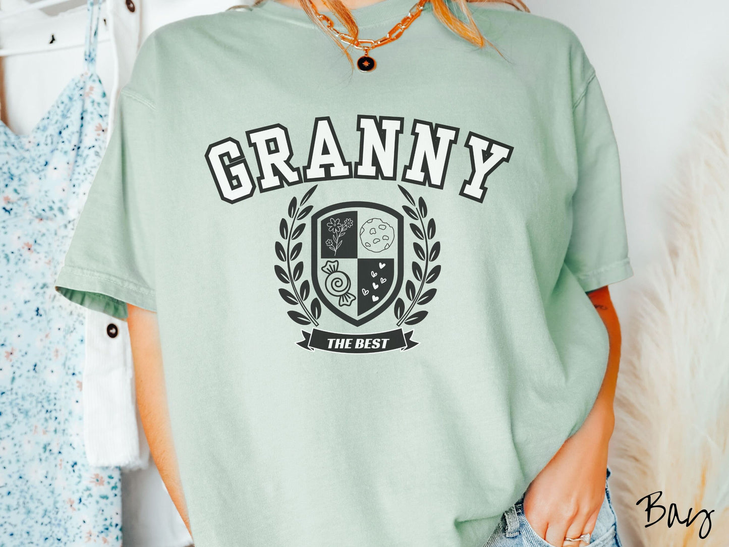 A woman wearing a cute bay colored shirt with text saying Granny across the front with a varsity logo underneath with the words The Best centered underneath the logo.