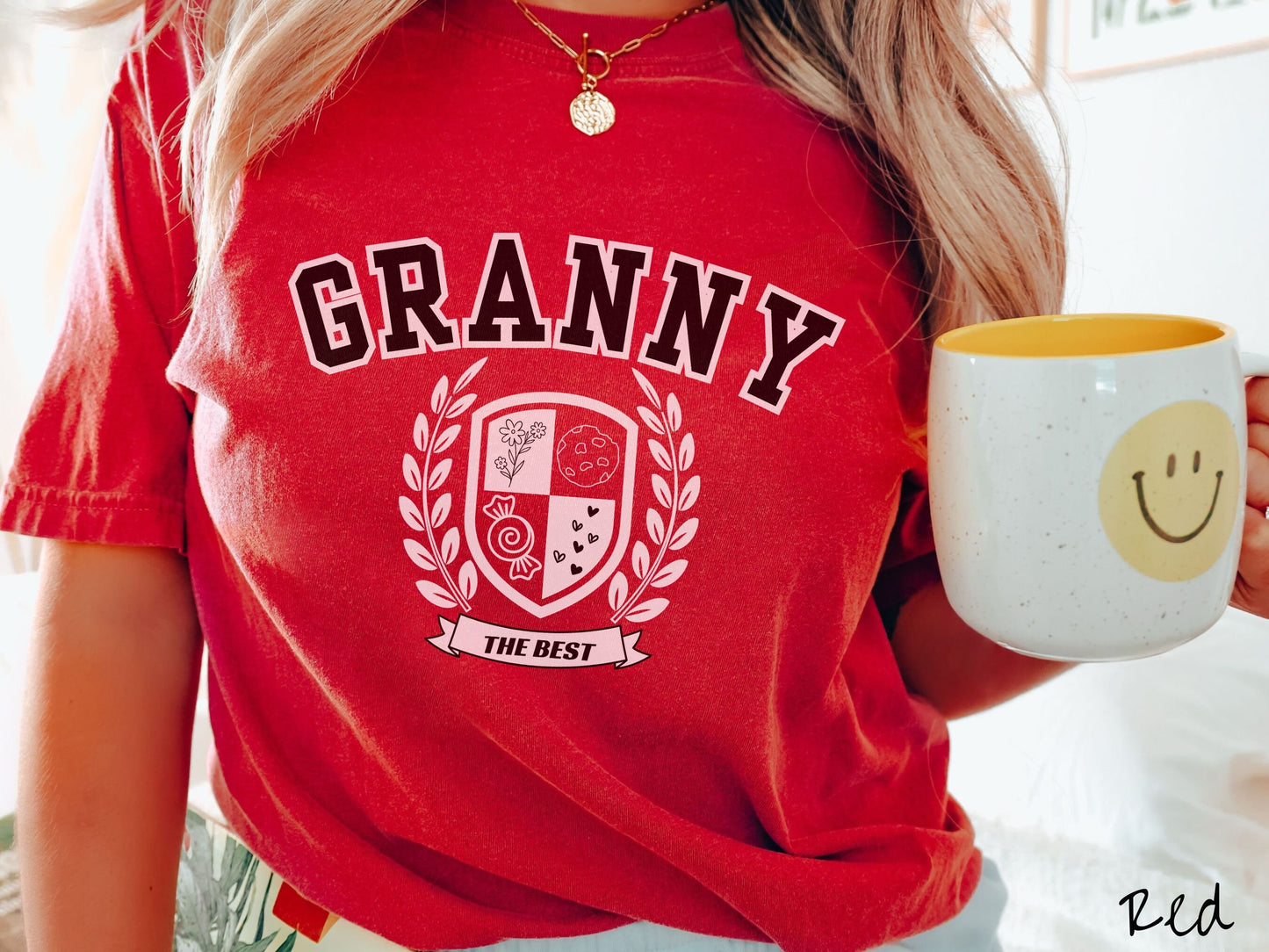 A woman wearing a cute red colored shirt with text saying Granny across the front with a varsity logo underneath with the words The Best centered underneath the logo.