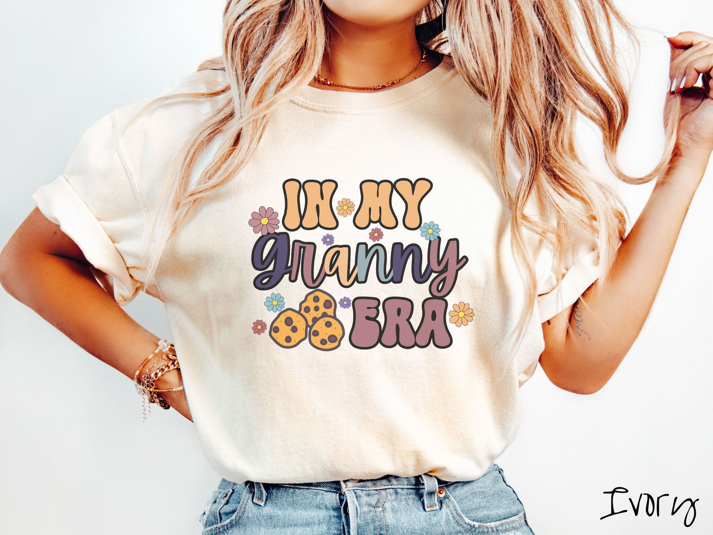 A woman wearing a cute ivory colored sweatshirt with text on the front saying In My Granny Era, with flowers and chocolate chip cookies mixed within the text.