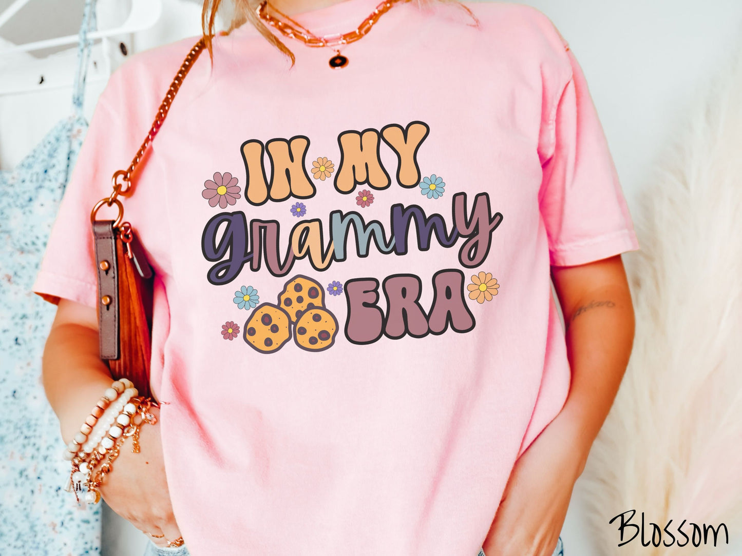 A woman wearing a cute pink shirt with the text saying In My Grammy era with flowers and chocolate chip cookies mixed within the text.