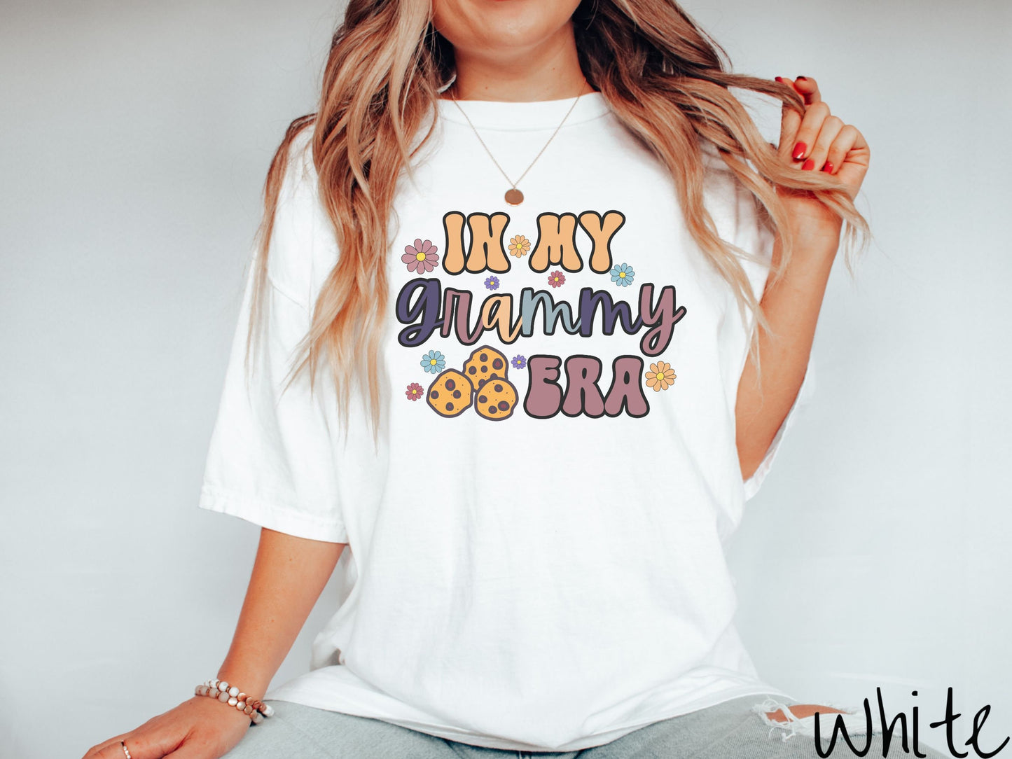 A woman wearing a cute, white shirt with the text saying In My Grammy era with flowers and chocolate chip cookies mixed within the text.