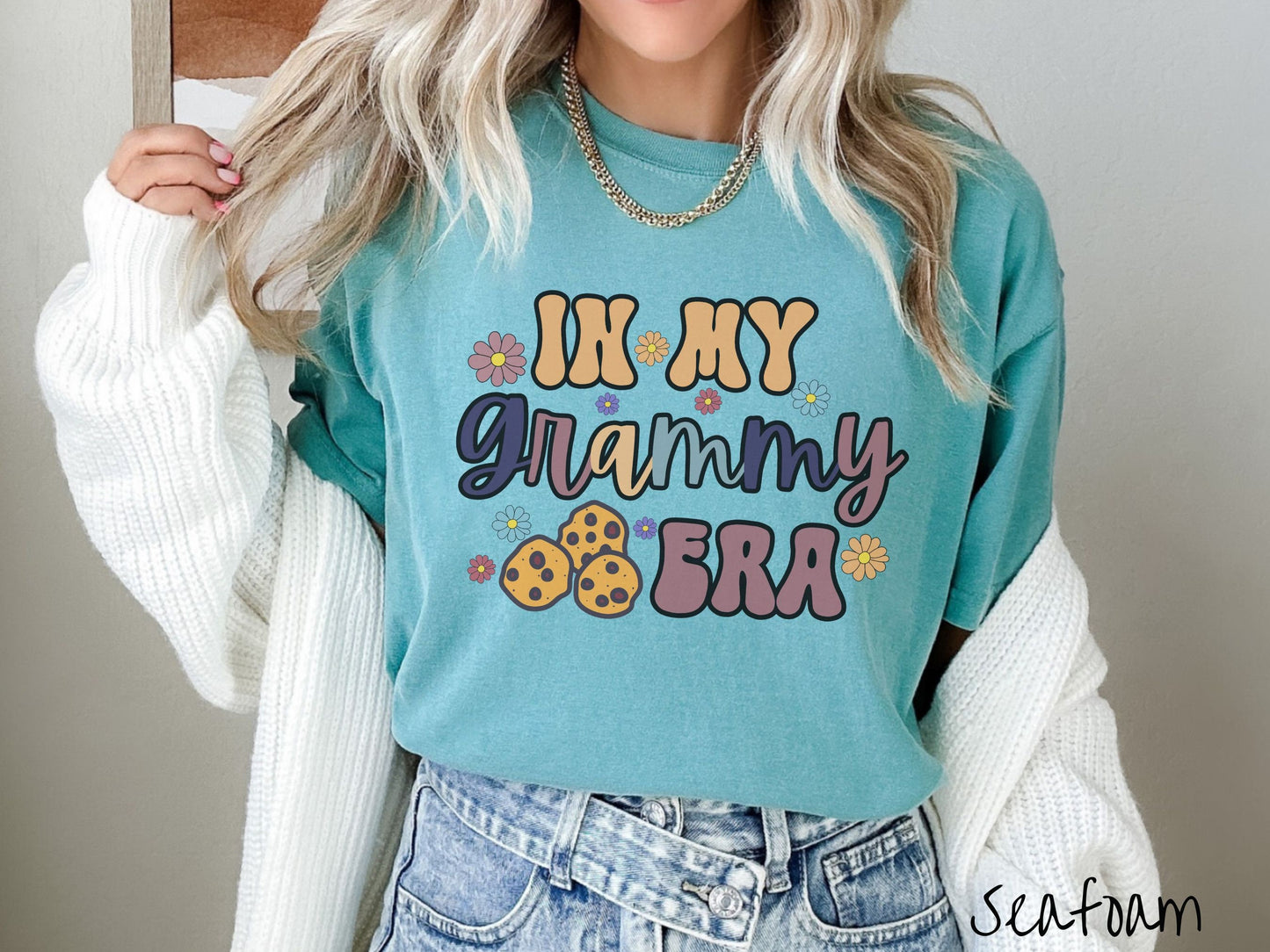 A woman wearing a cute cyan shirt with the text saying In My Grammy era with flowers and chocolate chip cookies mixed within the text.