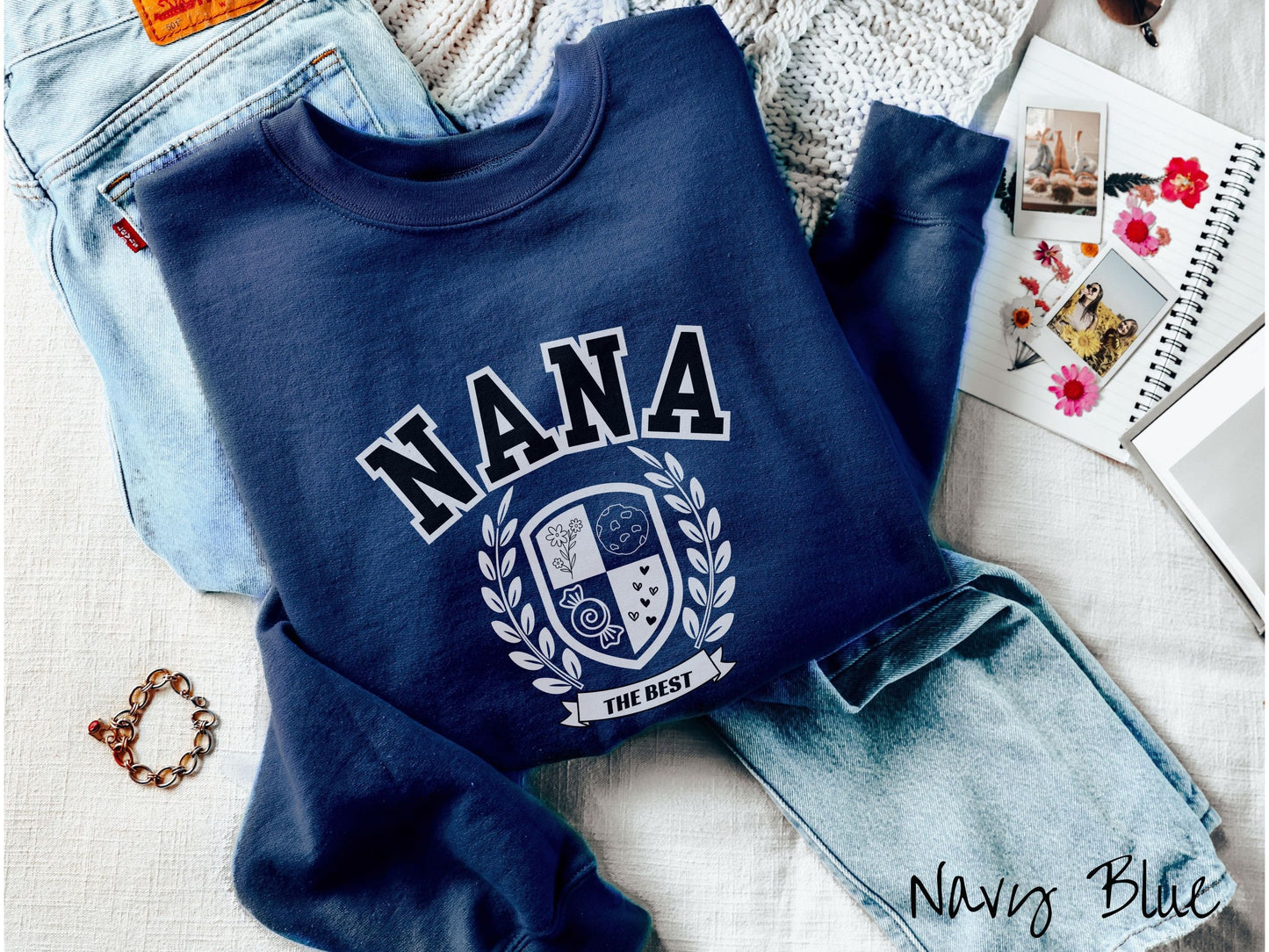 A woman wearing a cute navy blue colored sweatshirt with text saying Nana across the front with a varsity logo underneath with the words The Best centered underneath the logo.