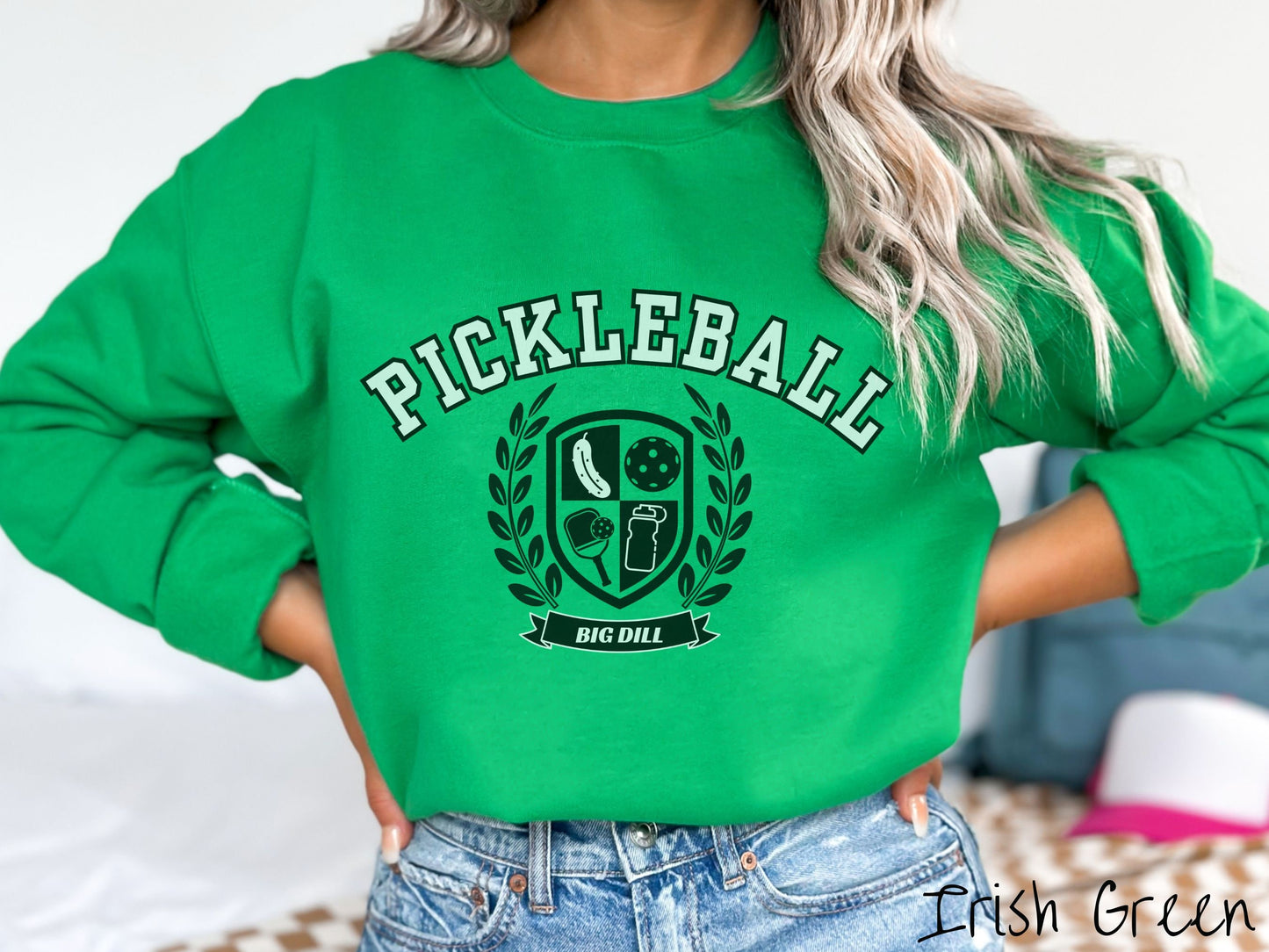 A woman wearing a cute Irish green colored sweatshirt with the text Pickleball across the top, a varsity logo centered underneath, and the words Big Dill underneath the logo.