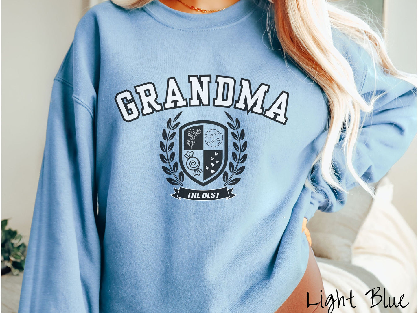 A woman wearing a cute light blue colored sweatshirt with text saying Grammy across the front with a varsity logo underneath with the words The Best centered underneath the logo.