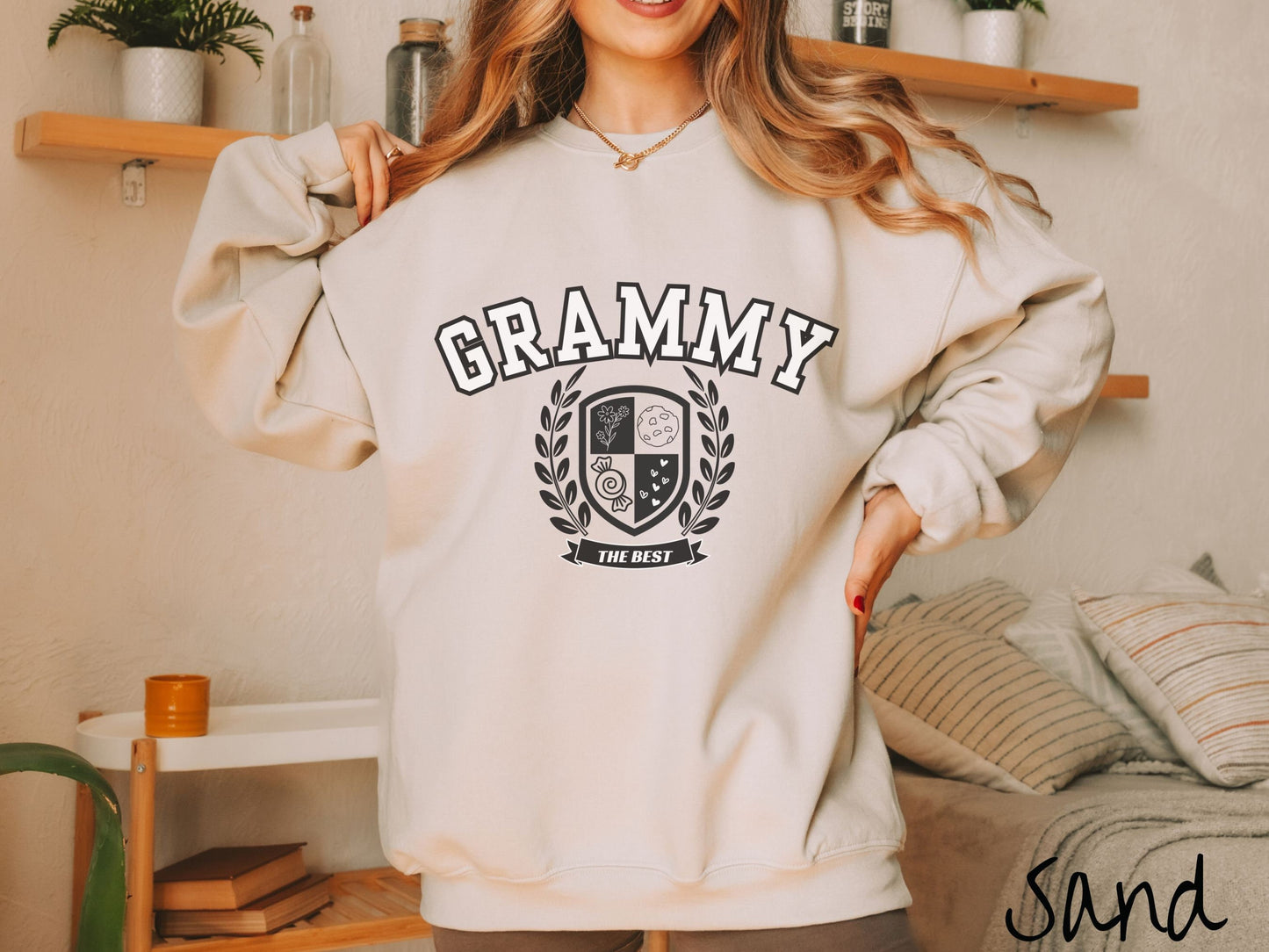 A woman wearing a cute sand colored sweatshirt with text saying Grammy across the front with a varsity logo underneath with the words The Best centered underneath the logo.