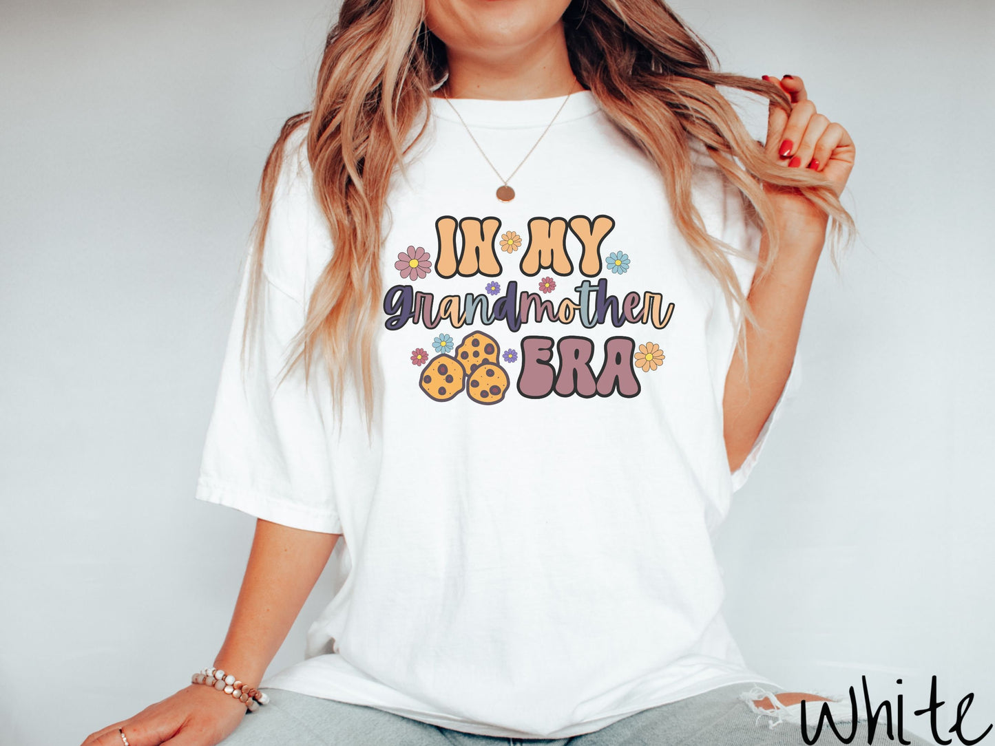 A woman wearing a cute white colored shirt with text on the front saying In My Grandmother Era, with flowers and chocolate chip cookies mixed within the text.