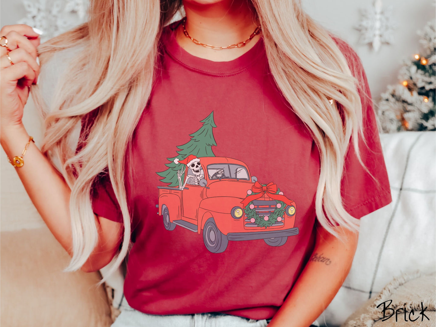 A woman wearing a cute, vintage brick colored comfy sweatshirt with a skeleton wearing a Christmas santa hat driving an old red pickup truck with a Christmas tree stuffed into the back, and a wreath across the front bumper.