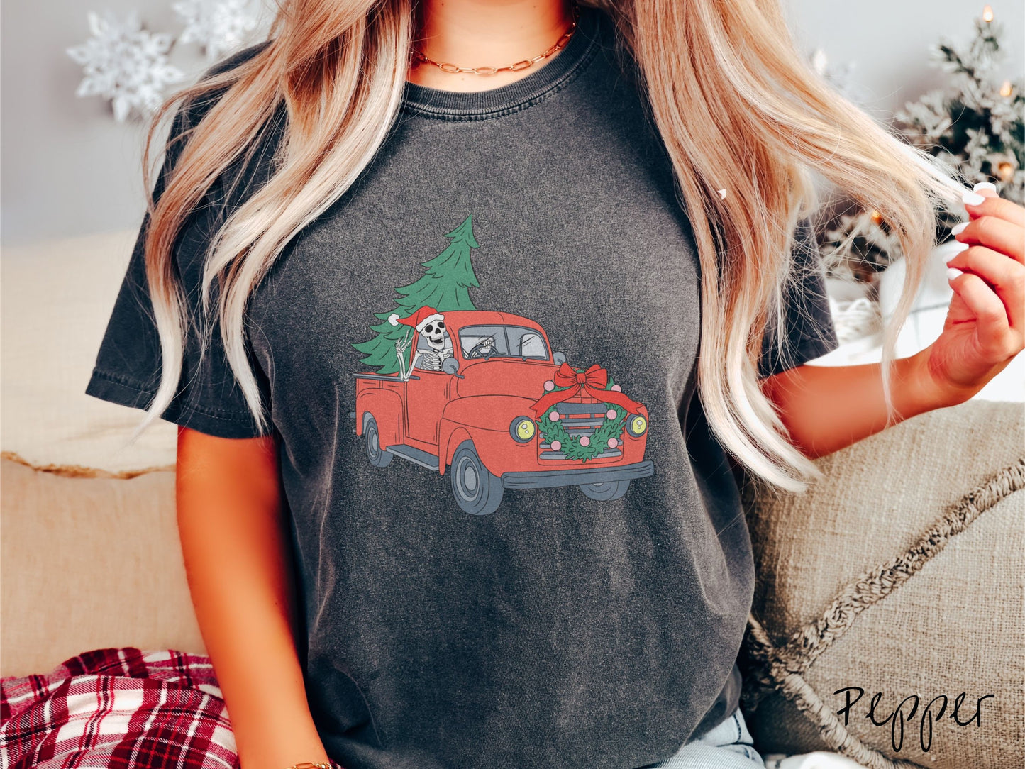 A woman wearing a cute, vintage pepper colored comfy sweatshirt with a skeleton wearing a Christmas santa hat driving an old red pickup truck with a Christmas tree stuffed into the back, and a wreath across the front bumper.