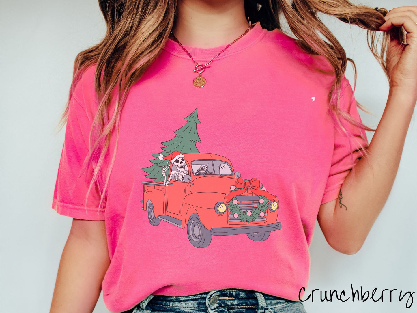 A woman wearing a cute, vintage crunchberry colored comfy sweatshirt with a skeleton wearing a Christmas santa hat driving an old red pickup truck with a Christmas tree stuffed into the back, and a wreath across the front bumper.