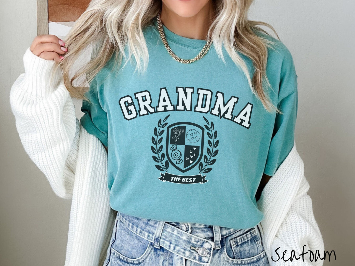 A woman wearing a cute seafoam colored shirt with text saying Grandma across the front with a varsity logo underneath with the words The Best centered underneath the logo.