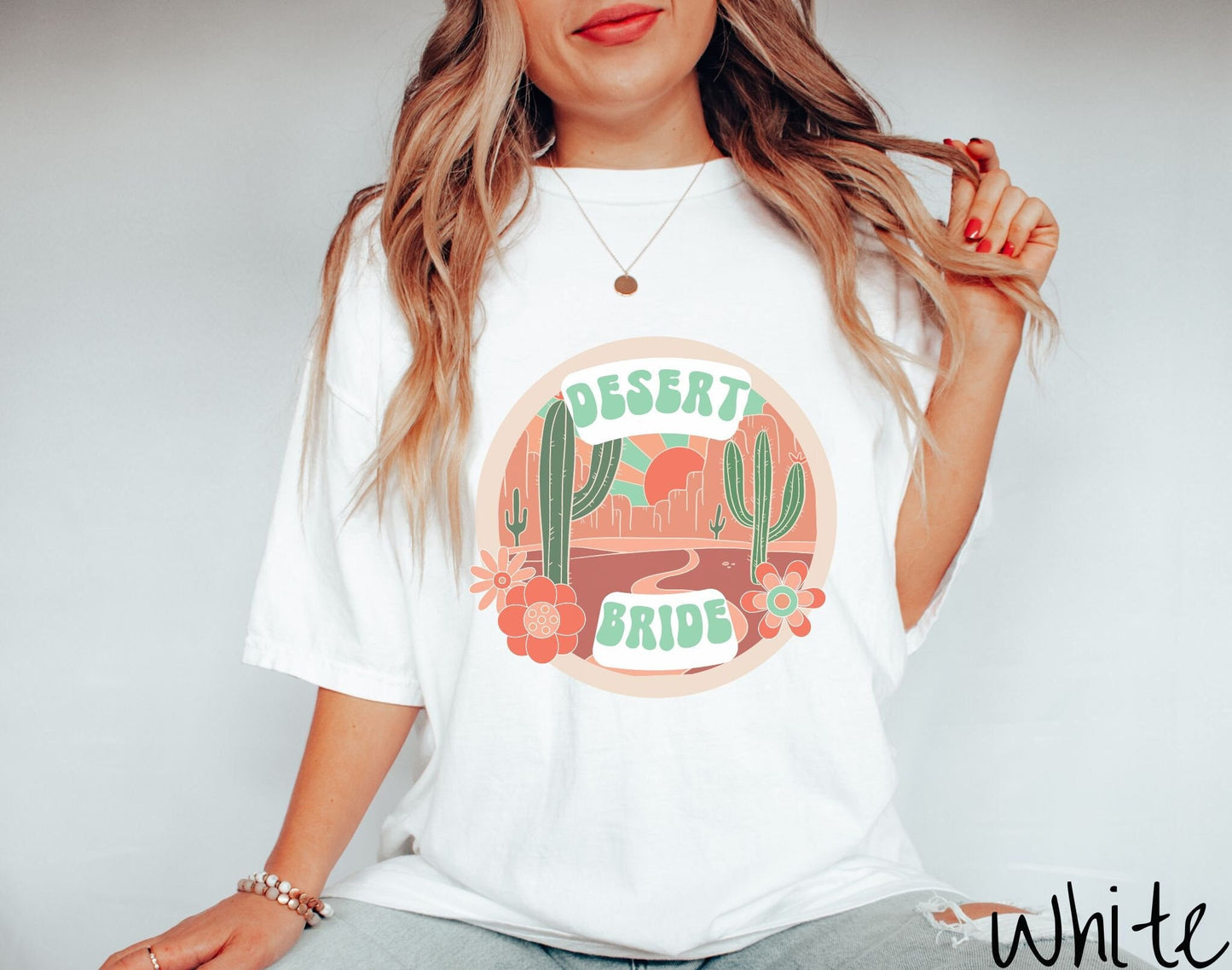 A woman wearing a cute white colored shirt with the text Desert Bride over an animated image of a desert road with cacti and desert flowers.