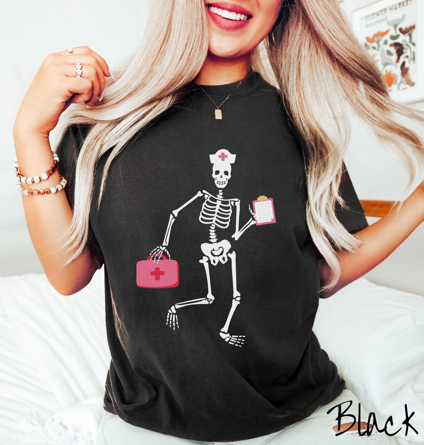A woman wearing a cute black colored shirt with a female skeleton dancing wearing a nurse’s hat and carrying a pink medical bag and a pink clipboard.