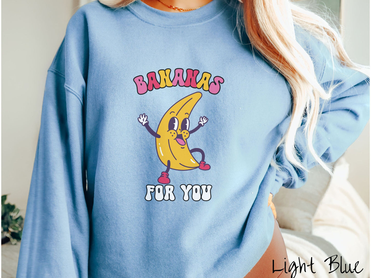 A woman wearing a cute, vintage light blue colored sweatshirt with the text Bananas for You in pink, red, purple, and white colors, and a cheerful banana with its arms open and a smiling face in the middle of the text.