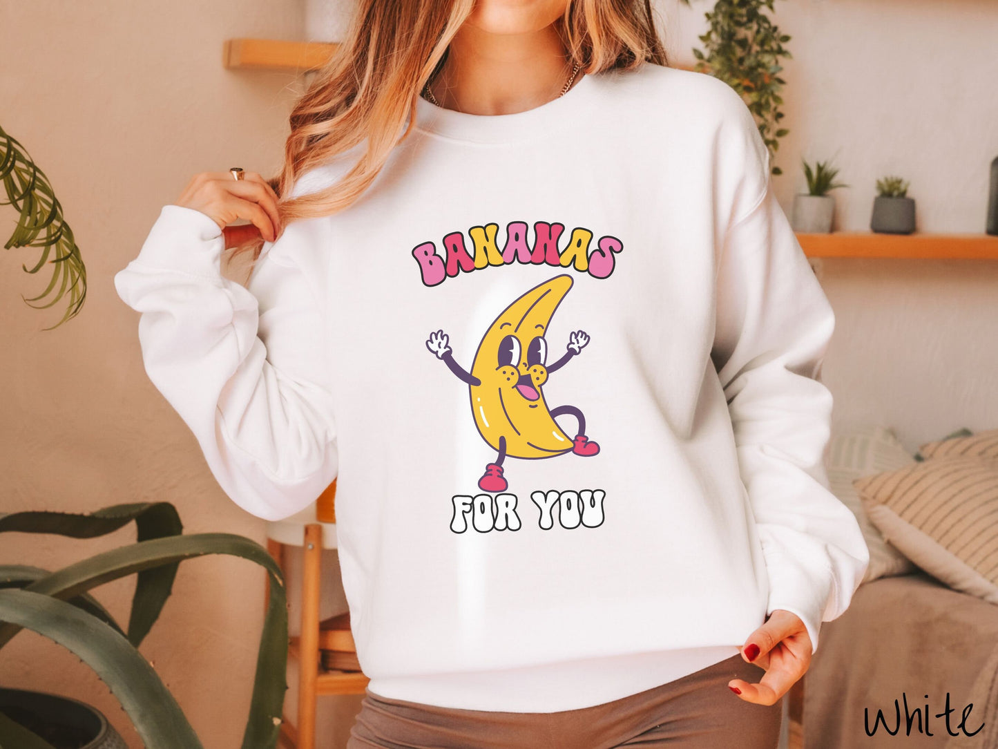 A woman wearing a cute, vintage white colored sweatshirt with the text Bananas for You in pink, red, purple, and white colors, and a cheerful banana with its arms open and a smiling face in the middle of the text.