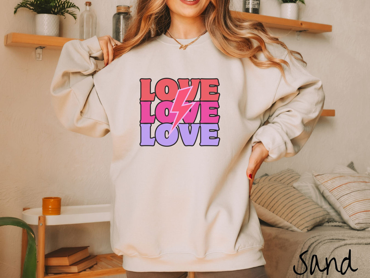 A woman wearing a cute, vintage sand colored sweatshirt with the word Love listed three times vertically with a pink lightning bolt going through the middle of the words.