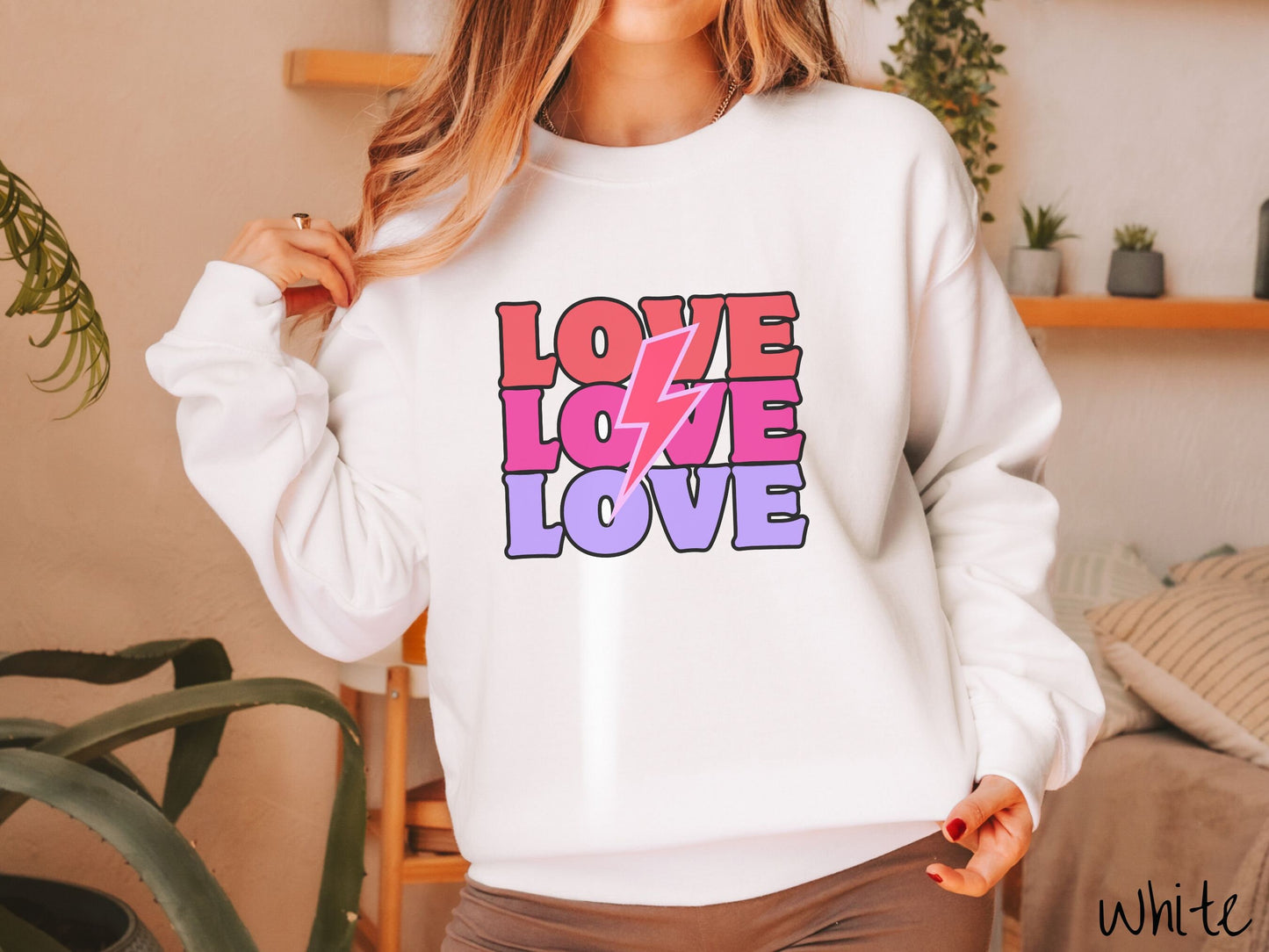 A woman wearing a cute, vintage white colored sweatshirt with the word Love listed three times vertically with a pink lightning bolt going through the middle of the words.
