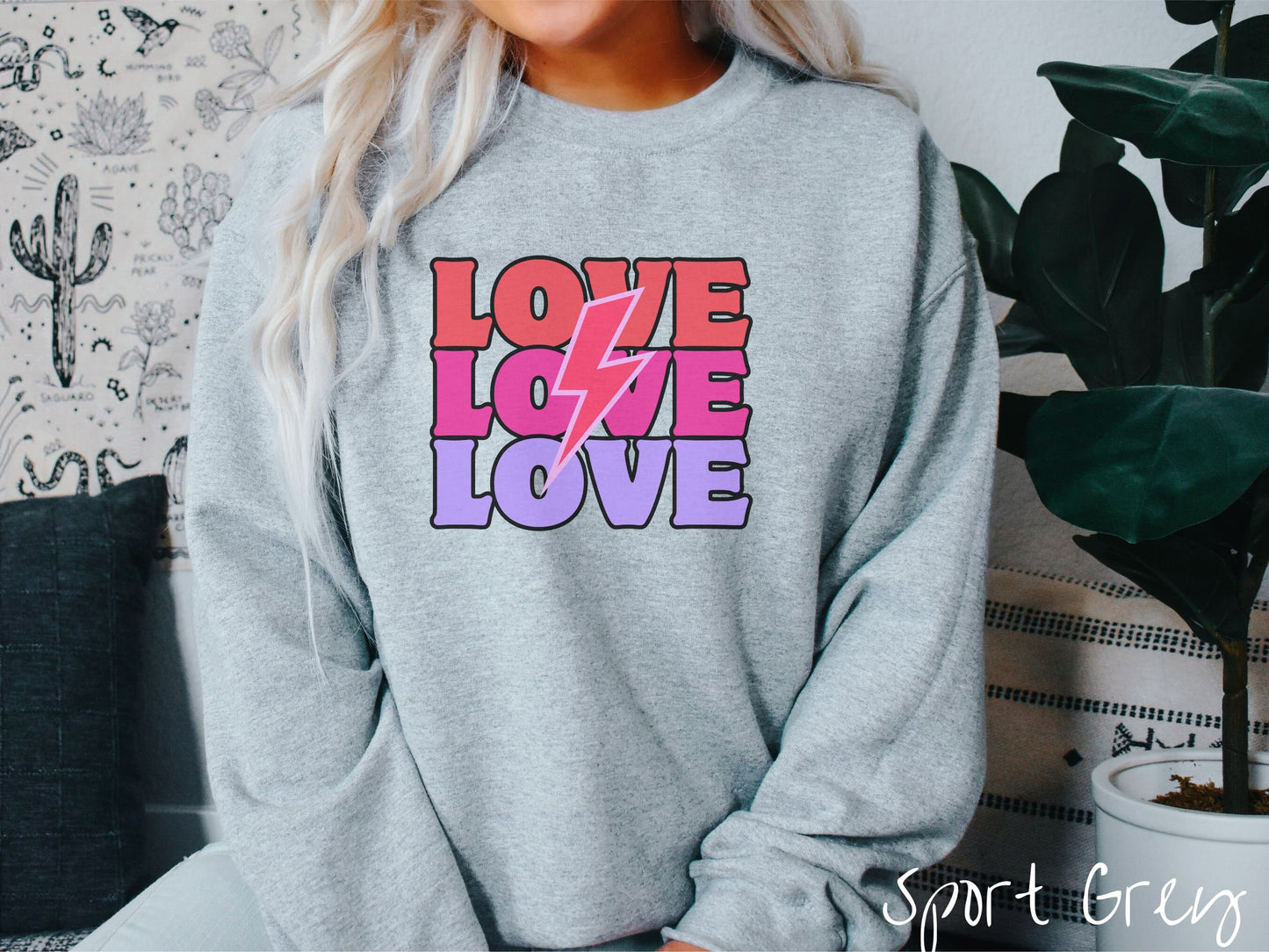 A woman wearing a cute, vintage sport grey colored sweatshirt with the word Love listed three times vertically with a pink lightning bolt going through the middle of the words.