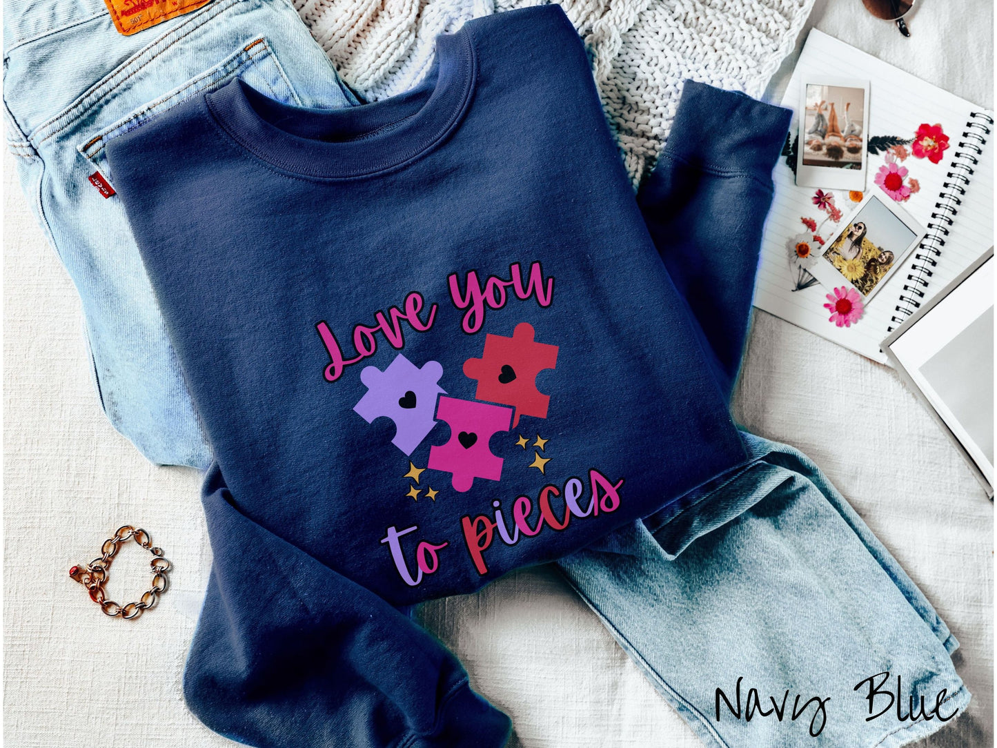 A cute, vintage navy blue colored sweatshirt with the text Love you to pieces in red, pink, and purple colors, and three red, pink, and purple puzzle pieces with hearts on them surrounded by yellow stars.