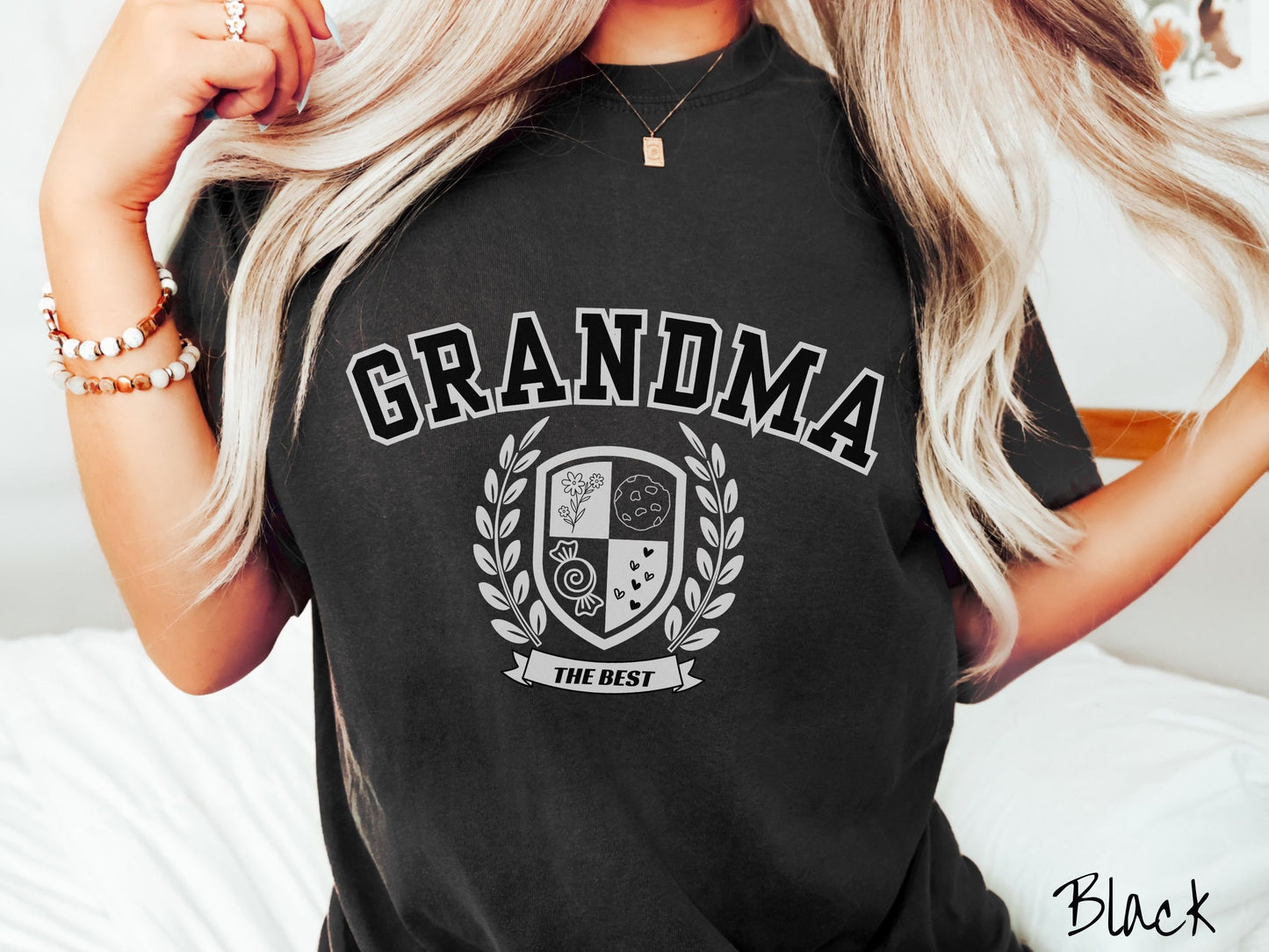 A woman wearing a cute black colored shirt with text saying Grandma across the front with a varsity logo underneath with the words The Best centered underneath the logo.