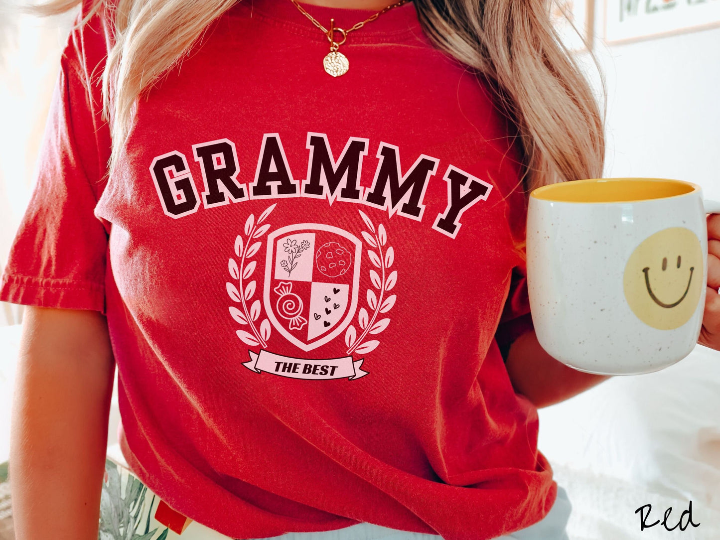 A woman wearing a cute red colored shirt with text saying Grammy across the front with a varsity logo underneath with the words The Best centered underneath the logo.
