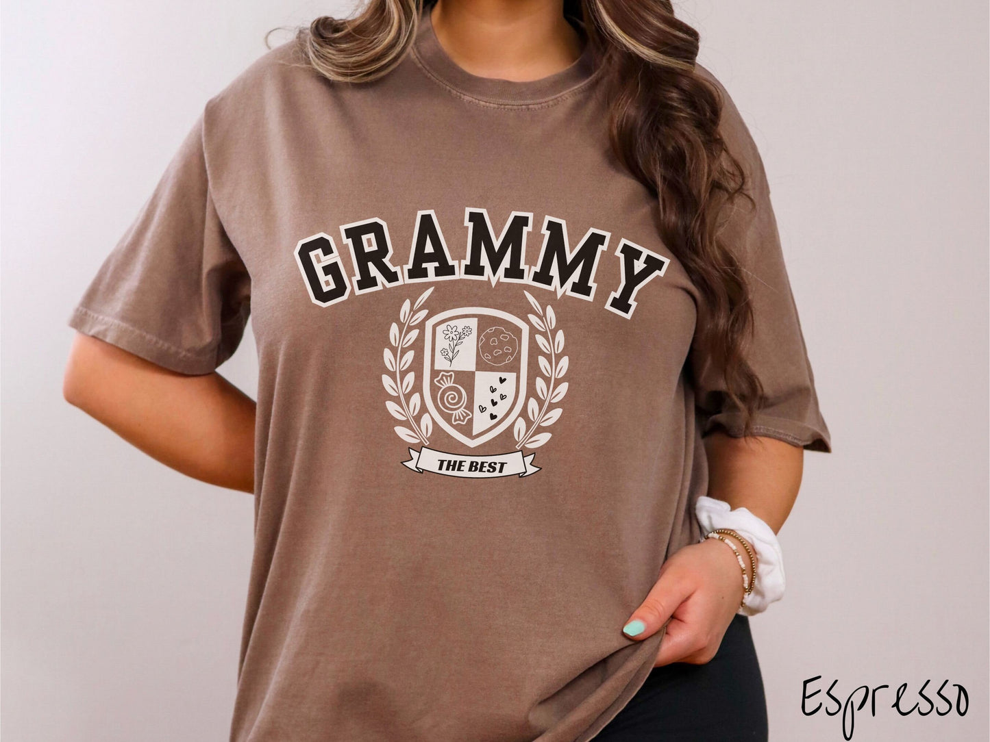 A woman wearing a cute espresso colored shirt with text saying Grammy across the front with a varsity logo underneath with the words The Best centered underneath the logo.