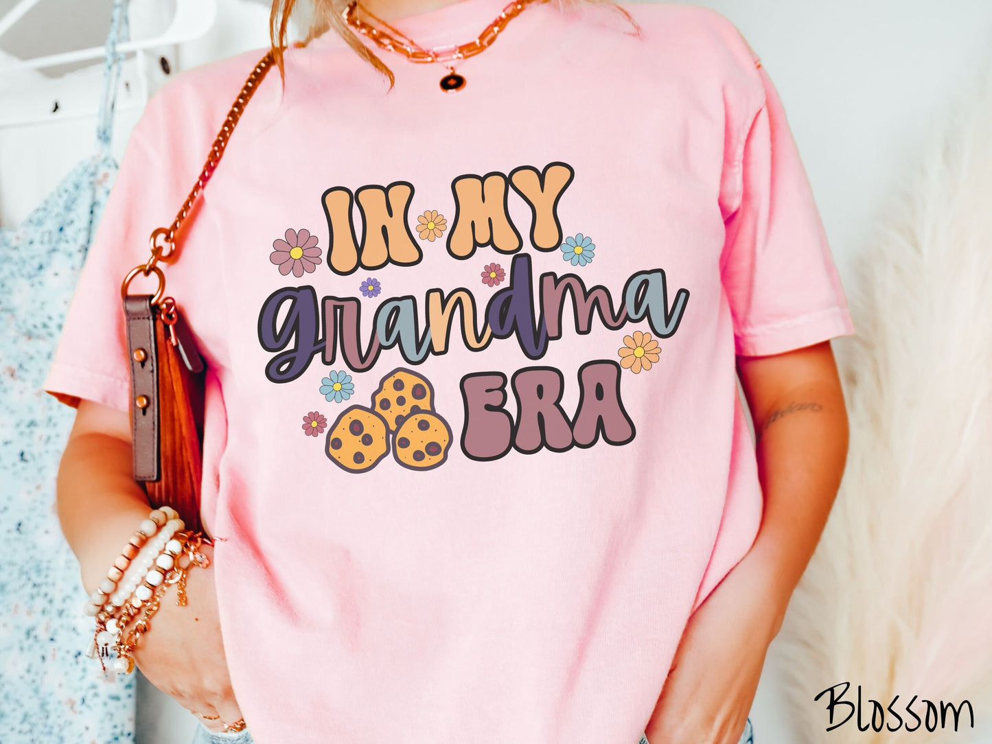 A woman wearing a cute pink shirt with the text saying In My Grandma era with flowers and chocolate chip cookies mixed within the text.