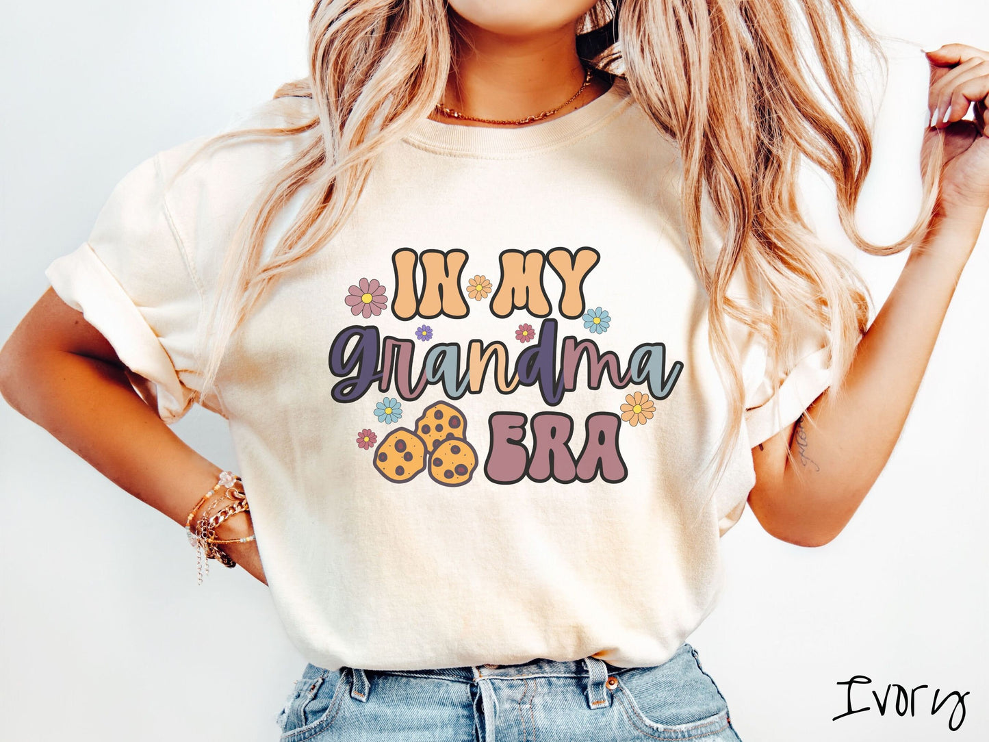 A woman wearing a cute cream shirt with the text saying In My Grandma era with flowers and chocolate chip cookies mixed within the text.