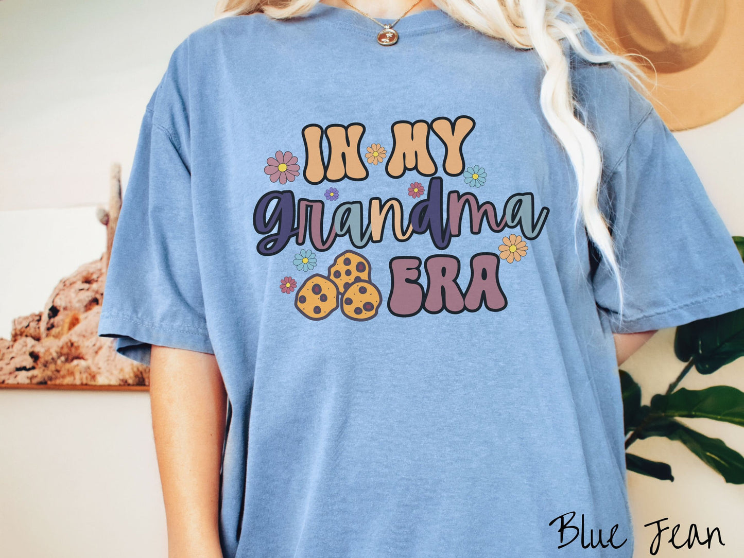 A woman wearing a cute blue shirt with the text saying In My Grandma era with flowers and chocolate chip cookies mixed within the text.